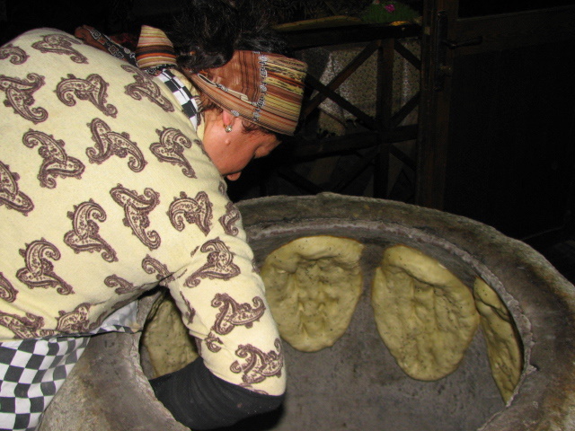 A lady checking the bread inside the tandyr